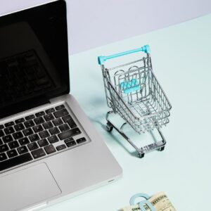 a macbook beside a miniature shopping cart and clipped money